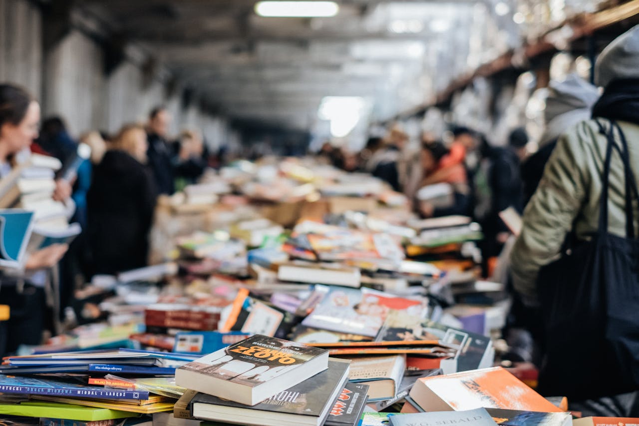 A bustling indoor book sale with numerous books and diverse people browsing.