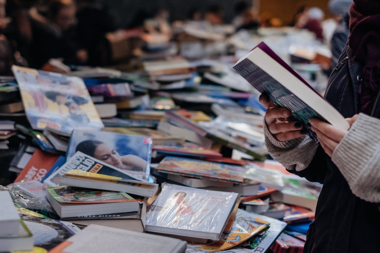A person browsing books at a crowded market book sale, offering a variety of genres and selections.